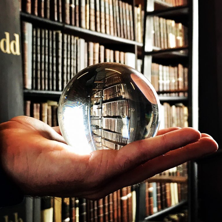 Glass ball in hand and old book shelves in the backgroun